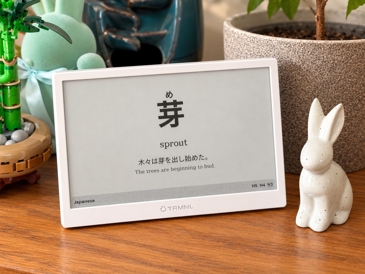 Kotoba running on a white TRMNL at home, showing 芽 with the reading め above it, the meaning "sprout", and a Japanese example sentence with its English translation.